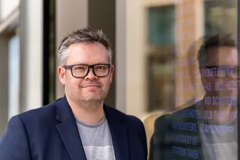 Alistair stood by a wall of glass with reflections and words on it