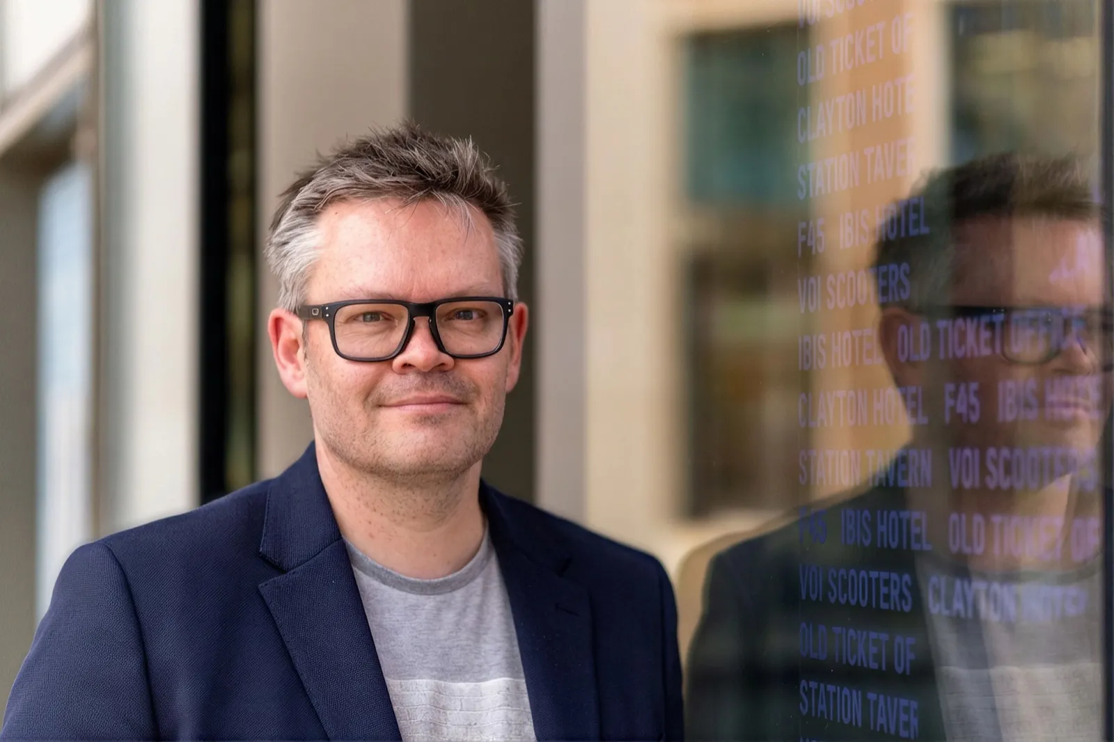 Alistair Stead standing by a wall of glass with reflections and words on it