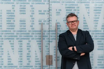Alistair Stead standing in front of a wall of glass with reflections and words on it